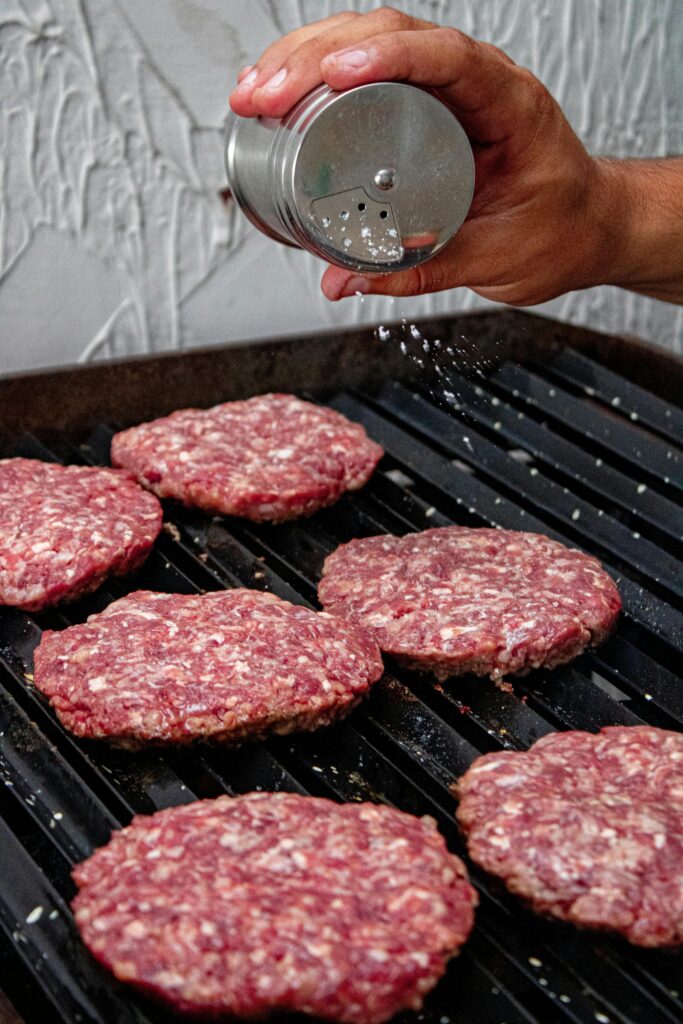 Raw ground venison burger recipe patties seasoned and grilling on a cast iron pan