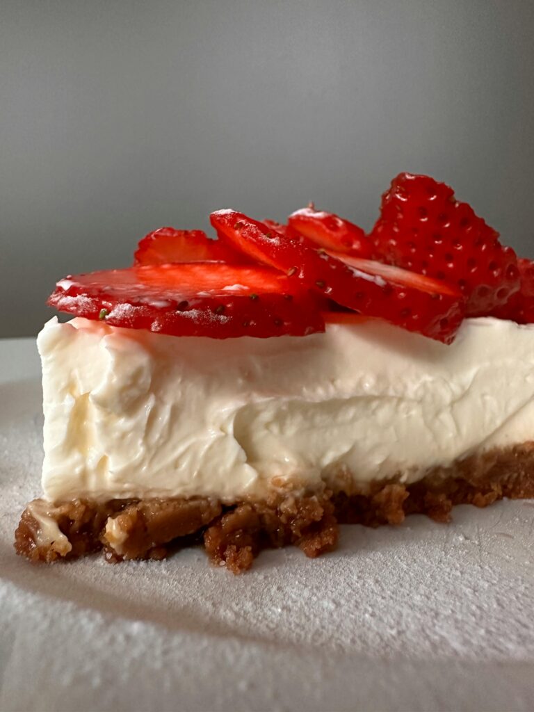 Homemade no-bake cheesecake recipe with berry topping and fresh strawberry on a heart plate.