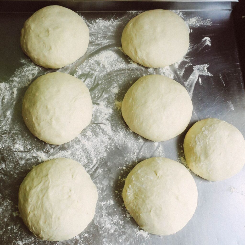 Soft easy homemade pizza dough balls resting on floured surface ready for shaping