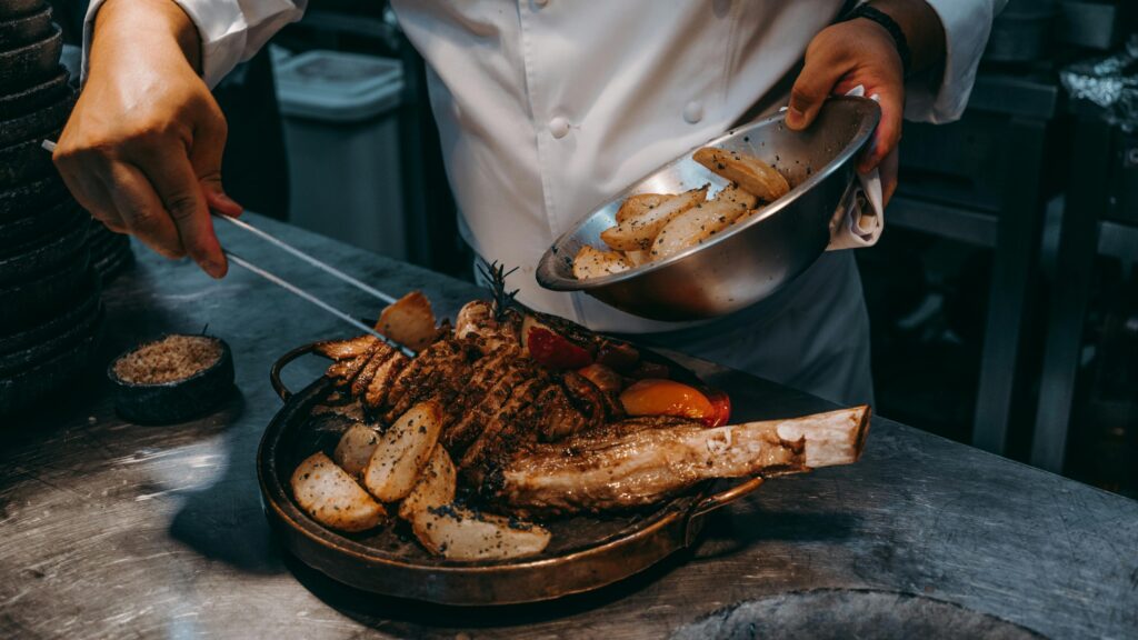 Chef serving juicy oven baked lamb leg roast with crispy roasted potatoes