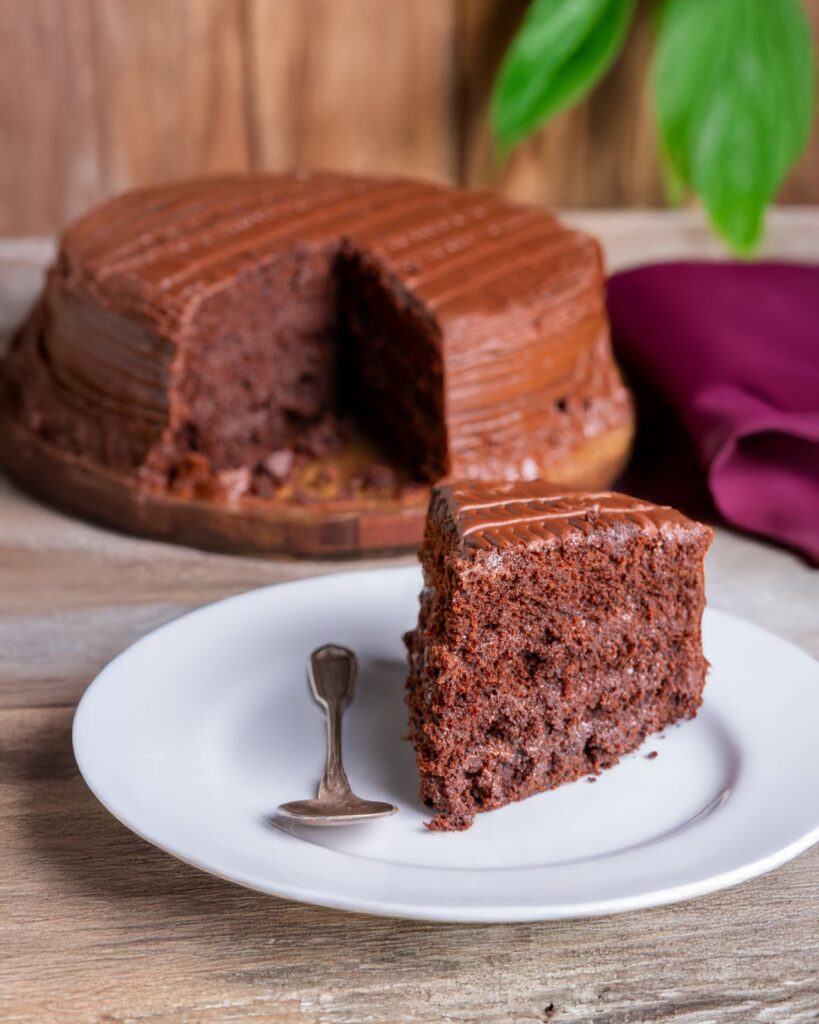 Eggless moist chocolate cake slice on a white plate with rich chocolate frosting and soft tender crumb