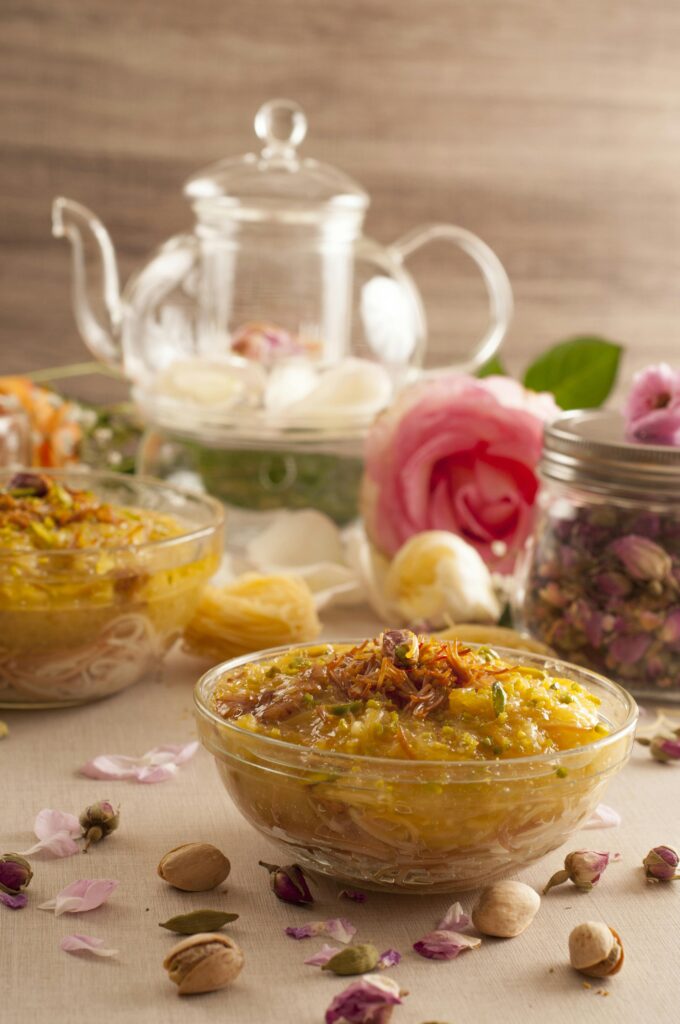 Festive Eid dessert table arrangement featuring traditional sweet dishes, a glass teapot, and decorative roses