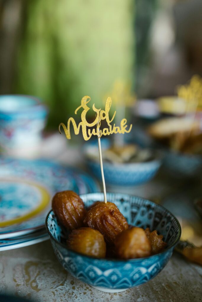 A blue ornate bowl containing various small fried desserts dipped in syrup, served on a festive table with an 'Eid Mubarak' topper, ideal for quick and easy no-bake Eid desserts for kids.