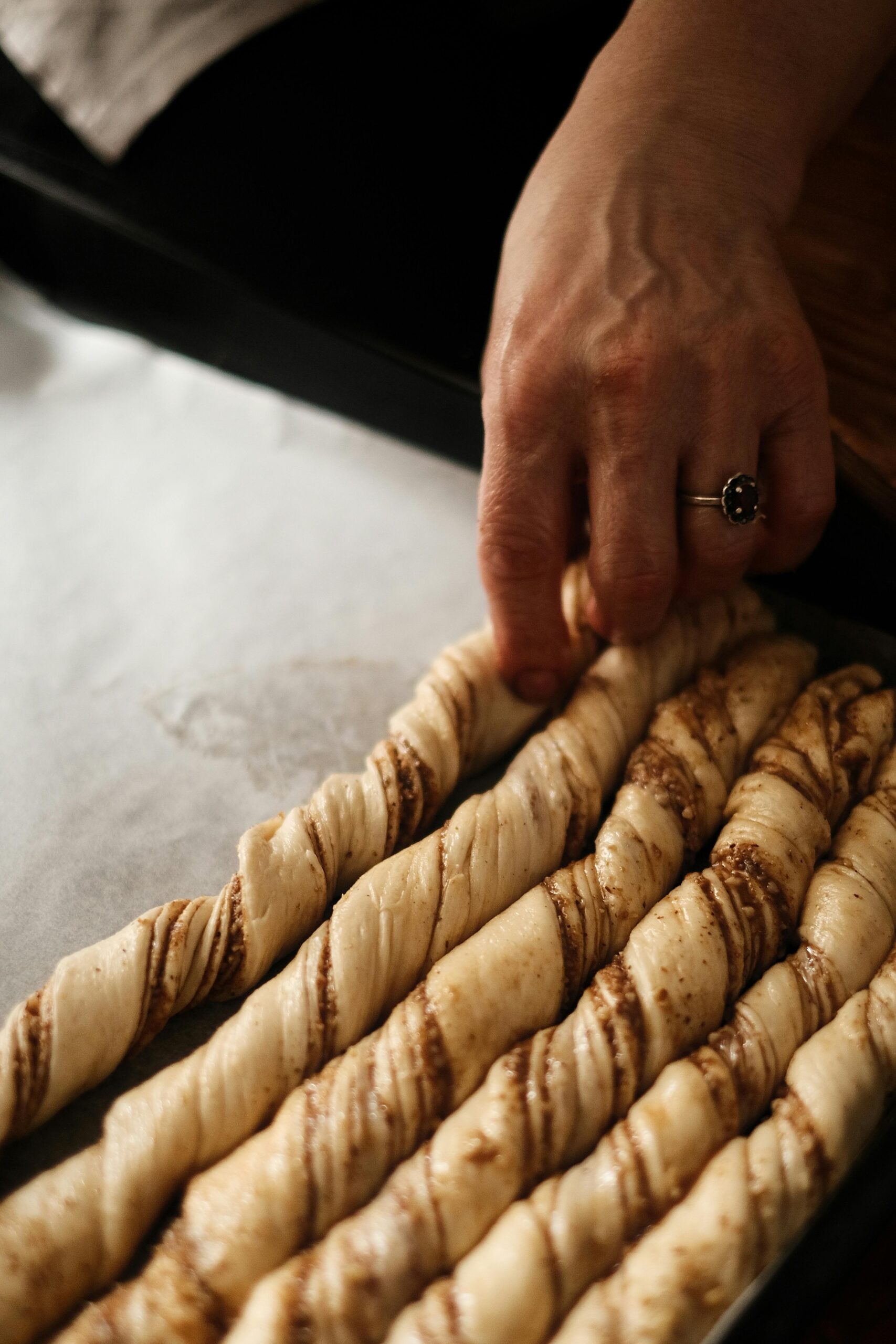 Baker rolling and twisting raw dough to make homemade Nutella puff pastry twists on a kitchen counter