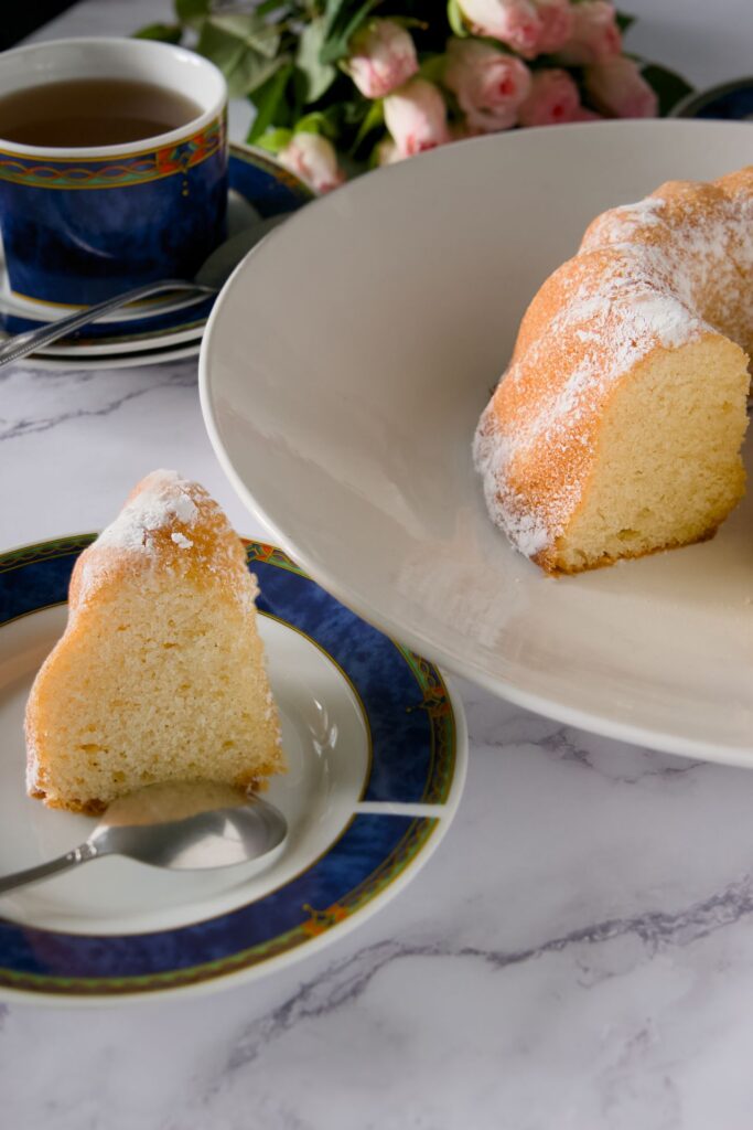 alt="Easy Vanilla Sponge Cake light and fluffy golden sponge cake sliced on wooden board with baking ingredients"