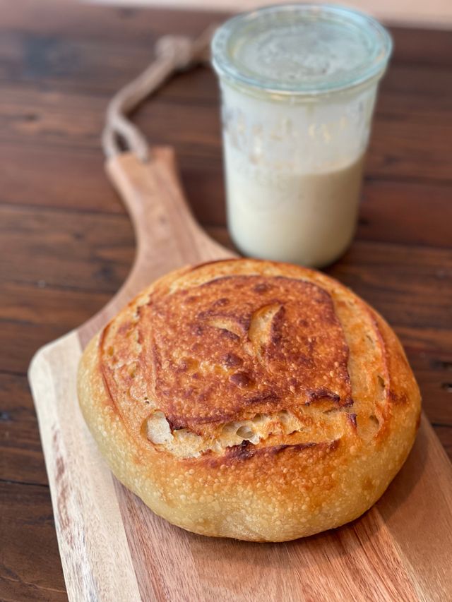 Rustic cardamom sourdough bread loaf served with a jug of milk on a wooden board